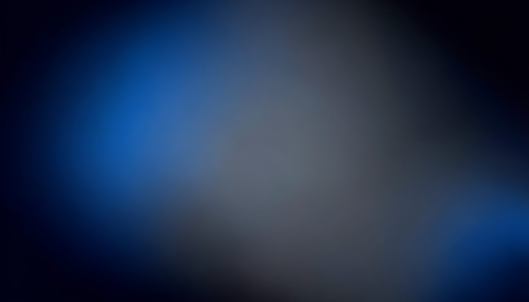 A dark abstract gradient composition shifting from deep navy at the edges into muted charcoal and soft slate at the center, with a quiet, contemplative mood.